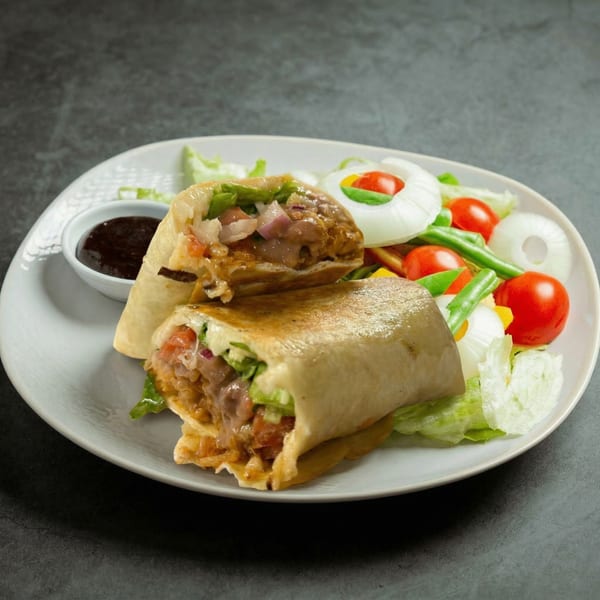 Mucho Loco Mexican Restaurant's burrito, cut in half, with a side salad and dipping sauce.